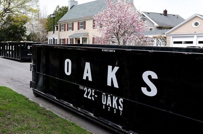 A large black dumpster with Oaks logo on residential street. Dumpster for waste collection.