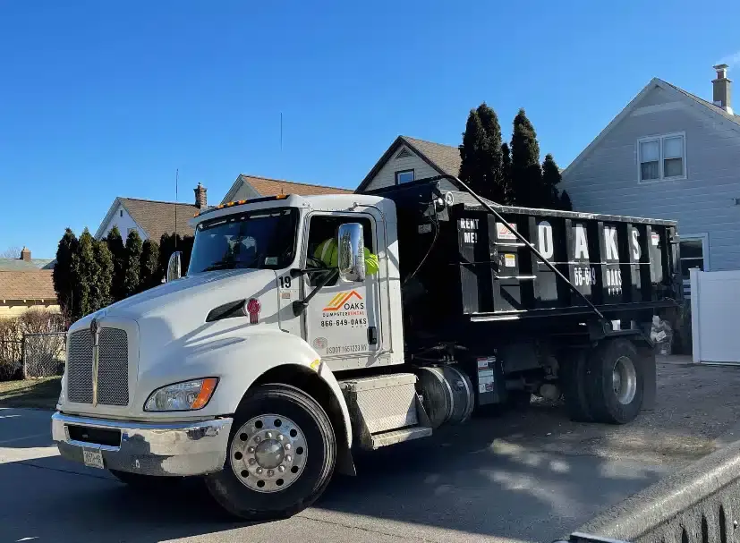 A large white dump truck parked on a suburban street. The truck has a black dumpster attached.