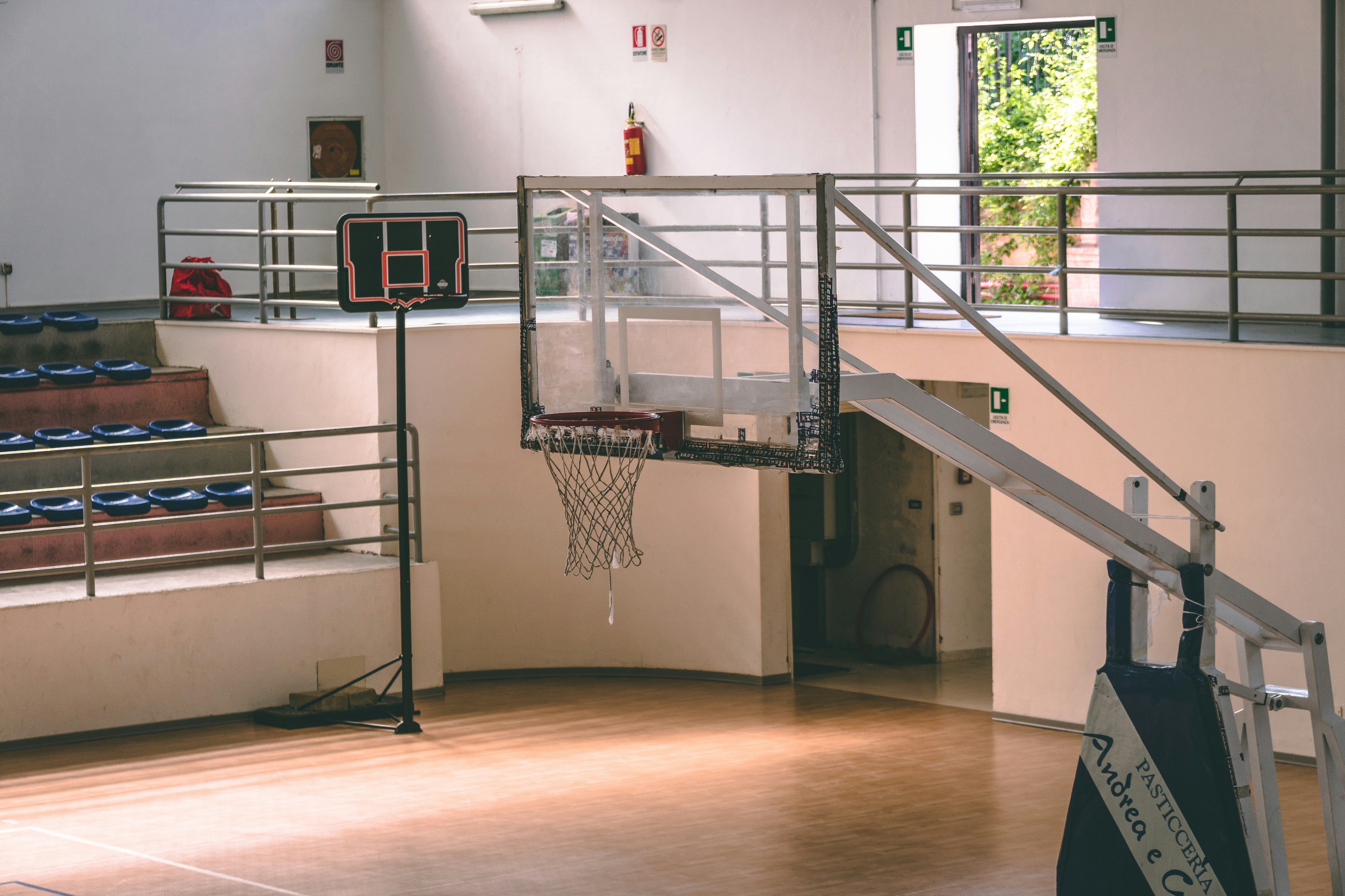 An indoor basketball court with a basketball hoop and seating area. A staircase leads to an upper level.