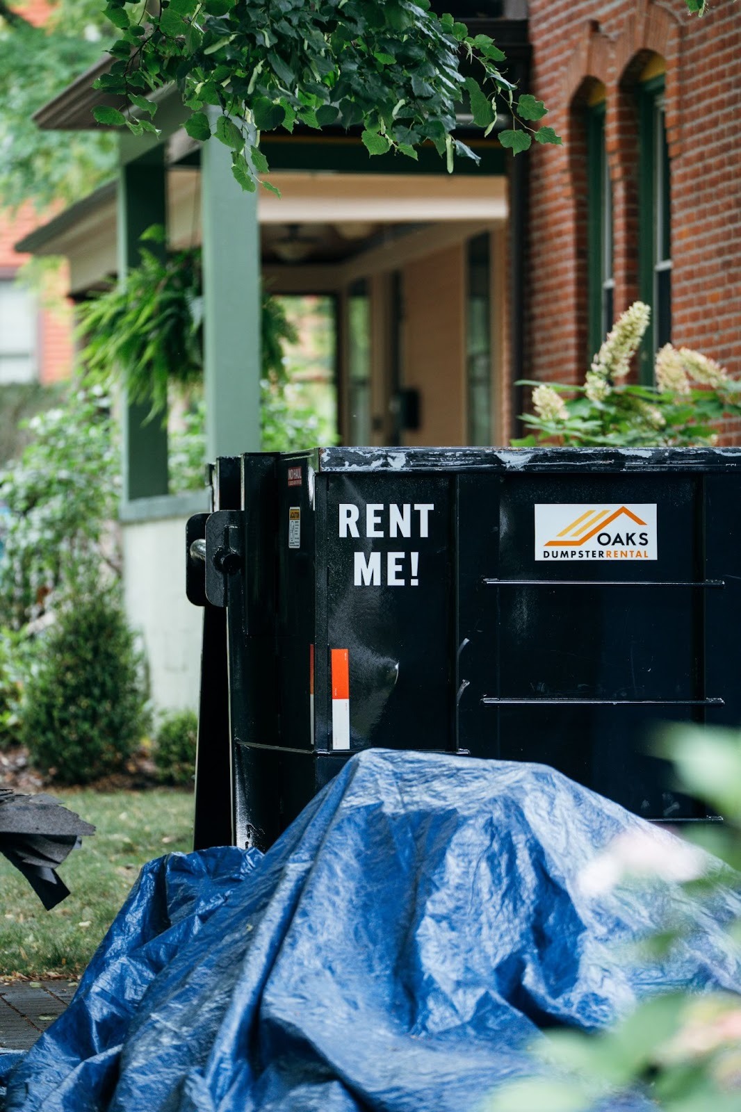 A black dumpster with a white sticker on the side. The dumpster has 'RENT ME!' written on it.
