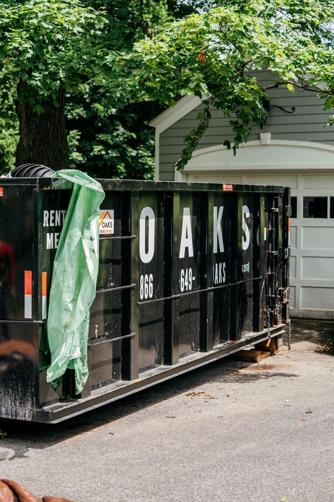 A large black dumpster with a green tarp hanging out