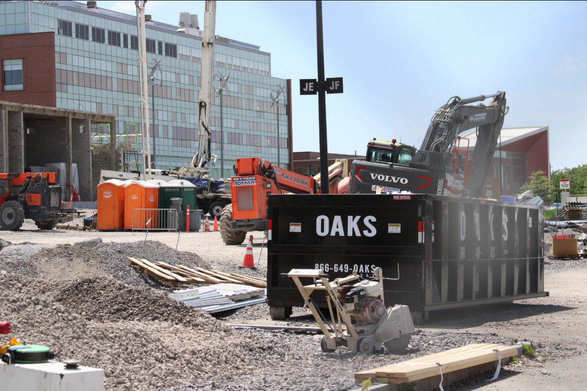 A dumpster and heavy machinery on a construction site. The dumpster has the word OAKS written on it.