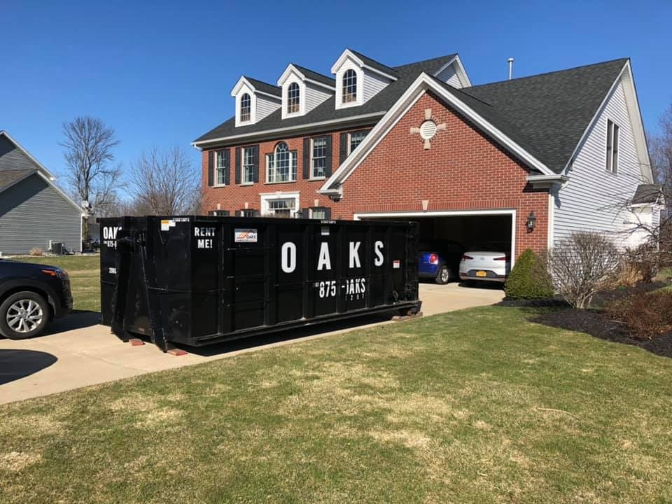 A large black dumpster with OAKS and a phone number on it