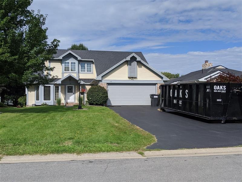 A house with a dumpster in the driveway. The house has a large front yard.