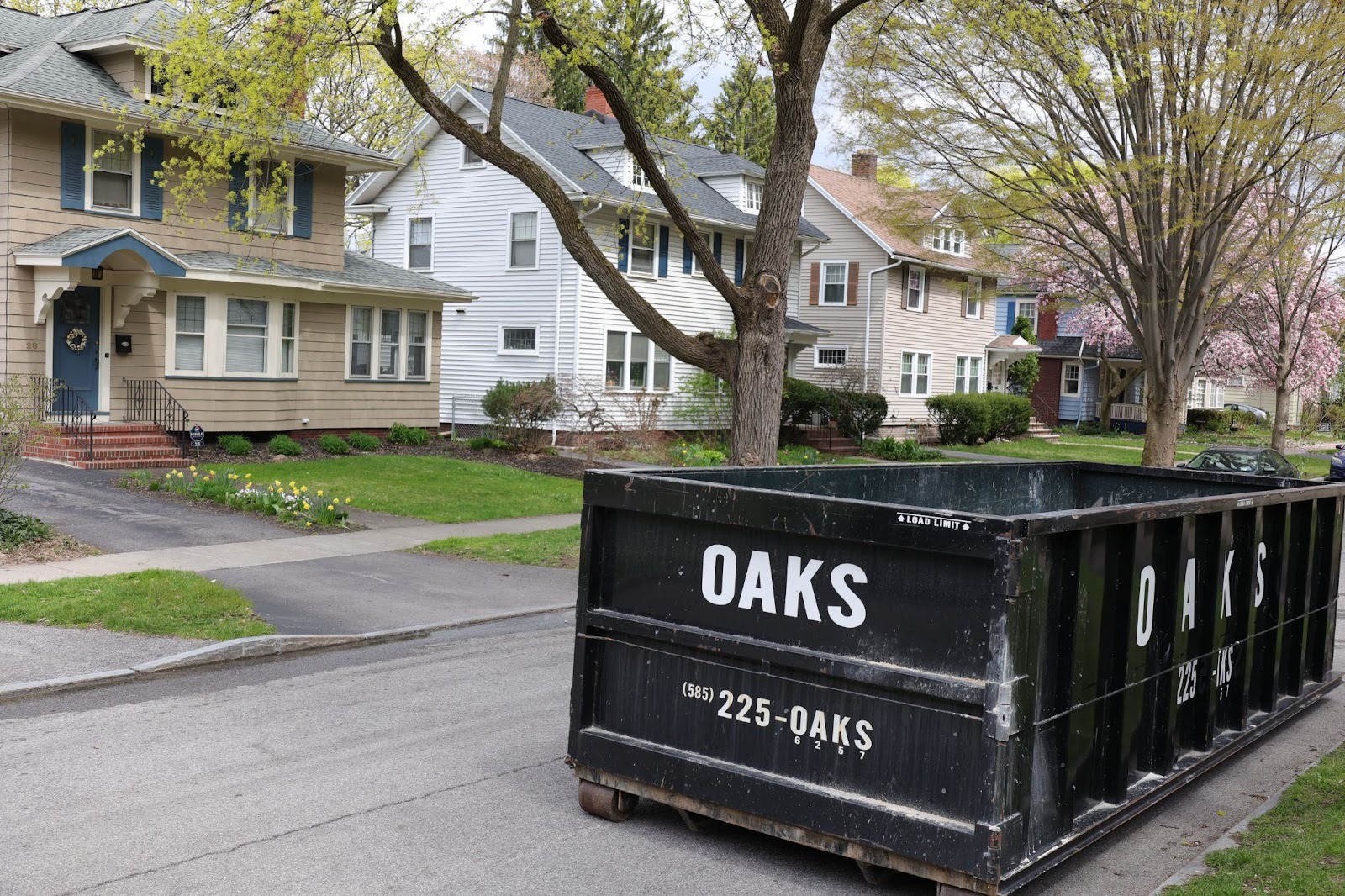 A large black dumpster on a residential street. Oaks dumpster rental services.