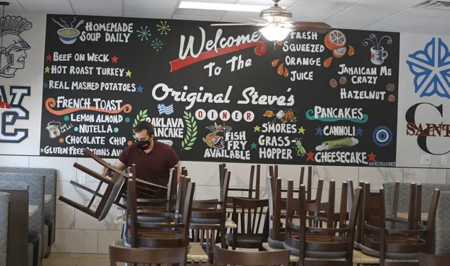 A sign on a wall with menu items listed. A person sitting at a table.