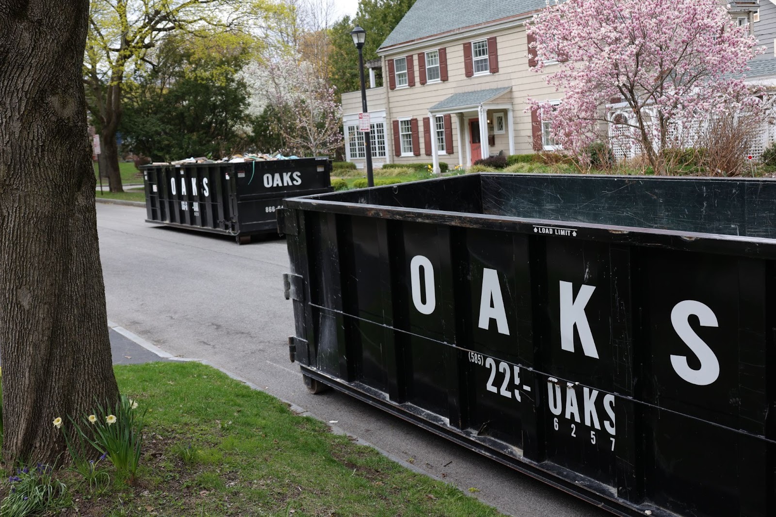 Two black dumpsters with 'OAKS' written on them.