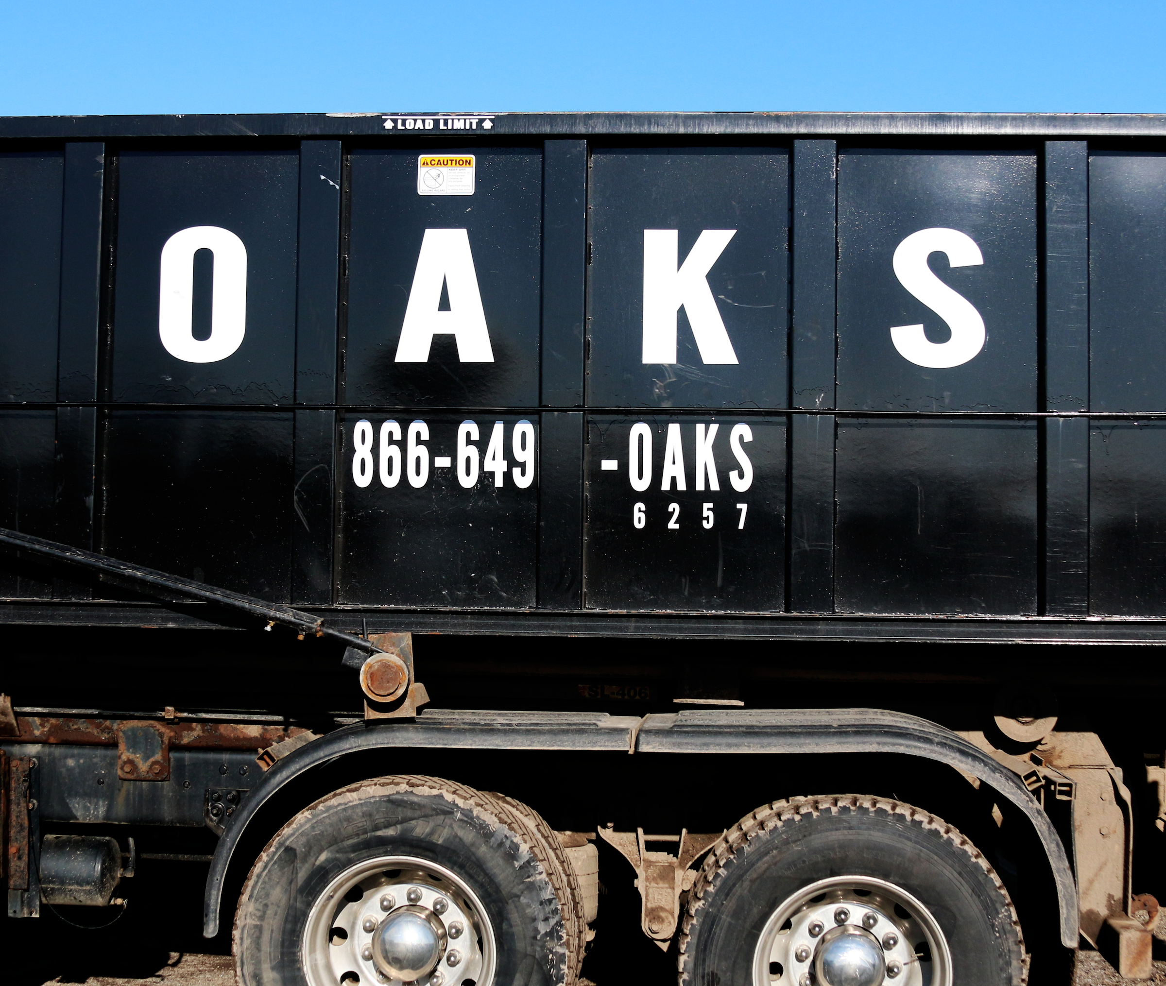 A black dump truck with the word OAKS and a phone number.
