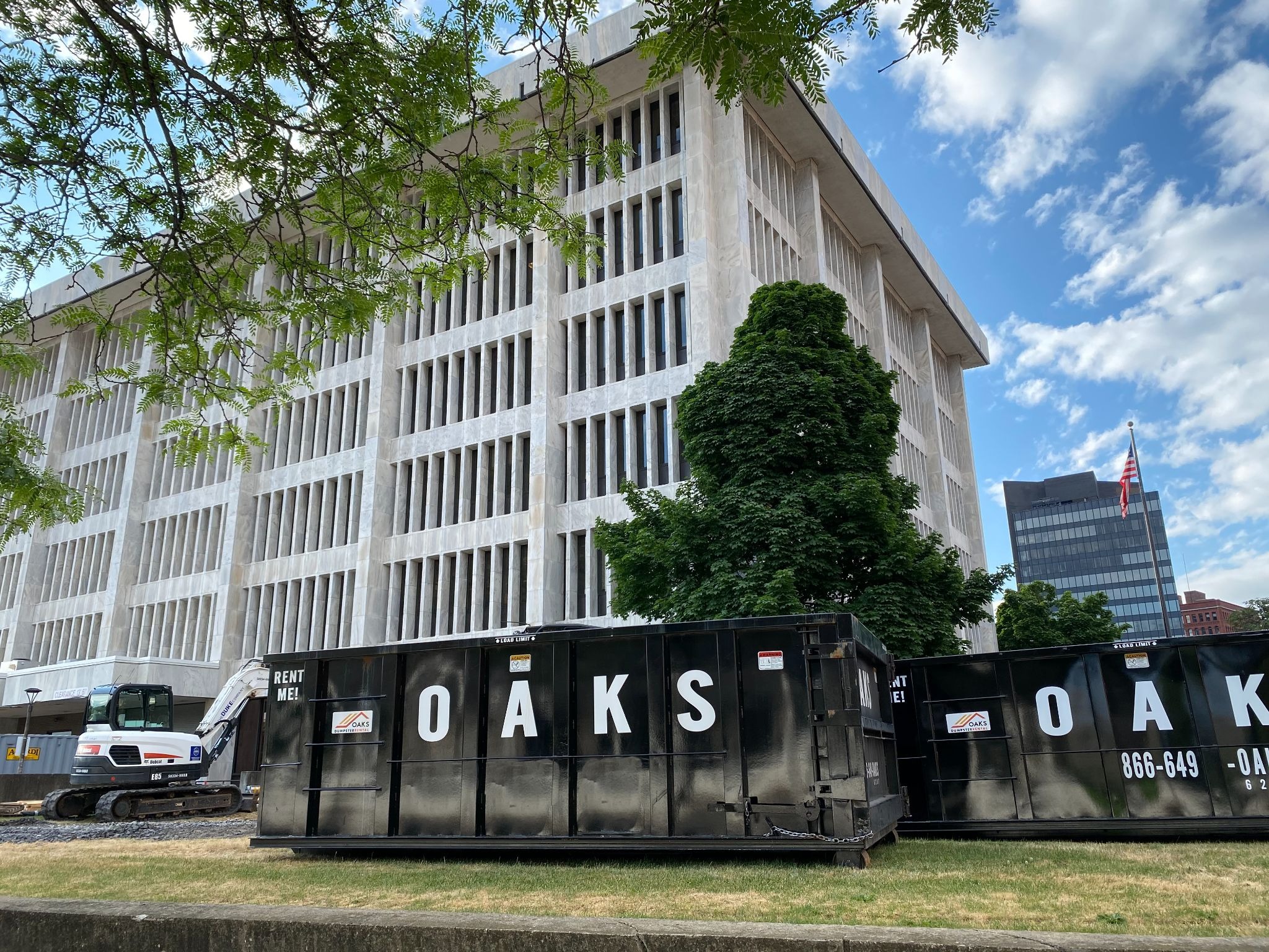 A large white building with a Oaks dumpster in the foreground. The dumpster is black with white lettering.