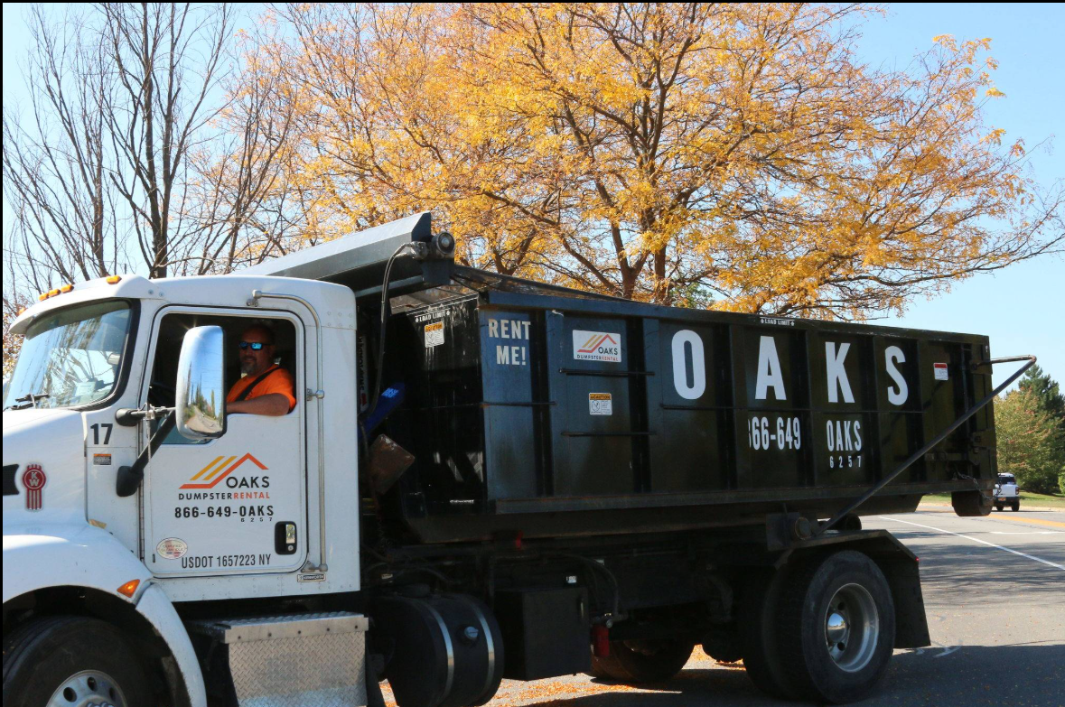 A white dump truck with a black dumpster on the back. Oaks logo on the side.
