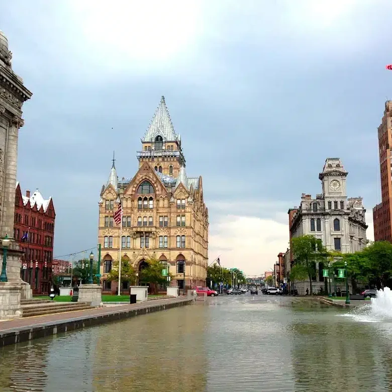 a large building with a clock tower and a fountain in front of it, with a statue on the left side of the image