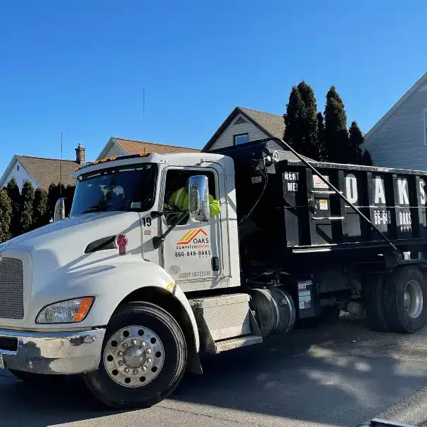 A large white dump truck parked on a suburban street. The truck has a black dumpster attached.