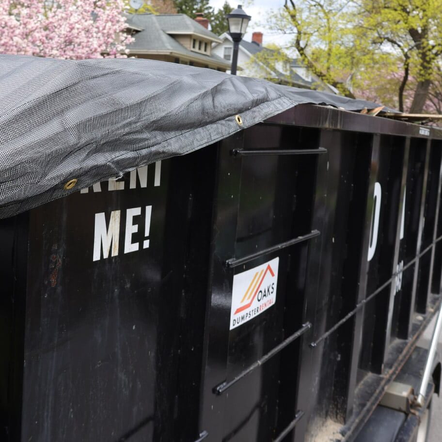 A black dumpster with a tarp cover sits on a residential street.