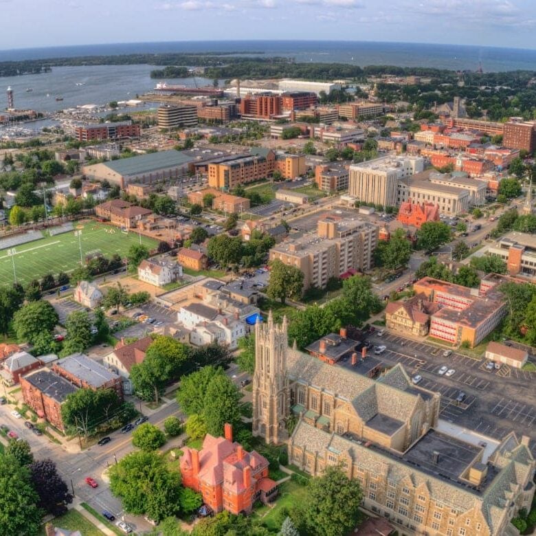 Aerial view of a university town by the water with a large church and football field.