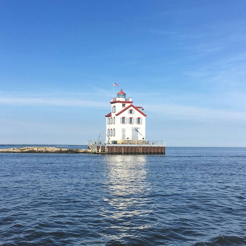A white lighthouse with red trim on a small island