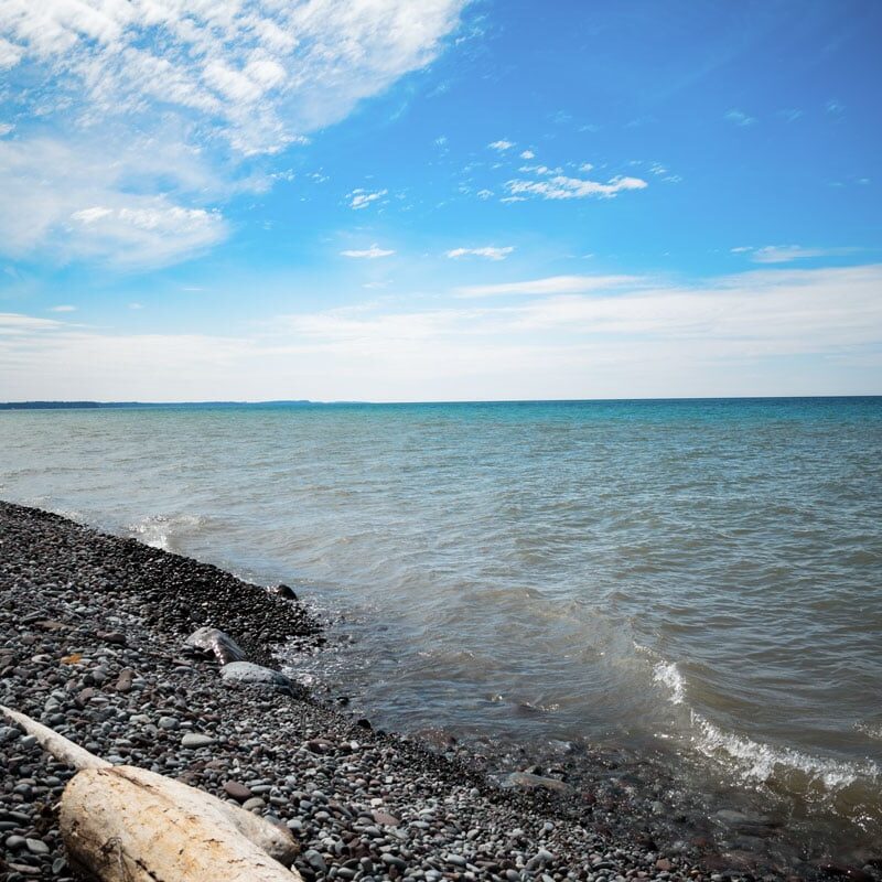 a lake shore with a blue sky and clouds