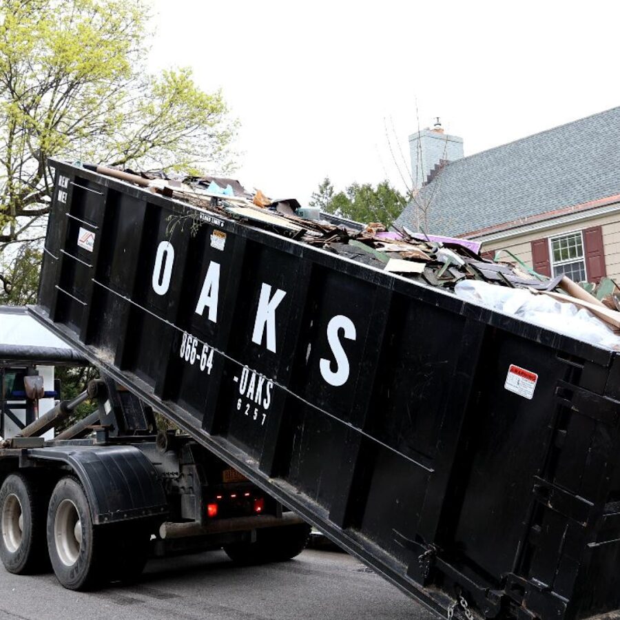 A black dumpster on a truck being emptied on a street