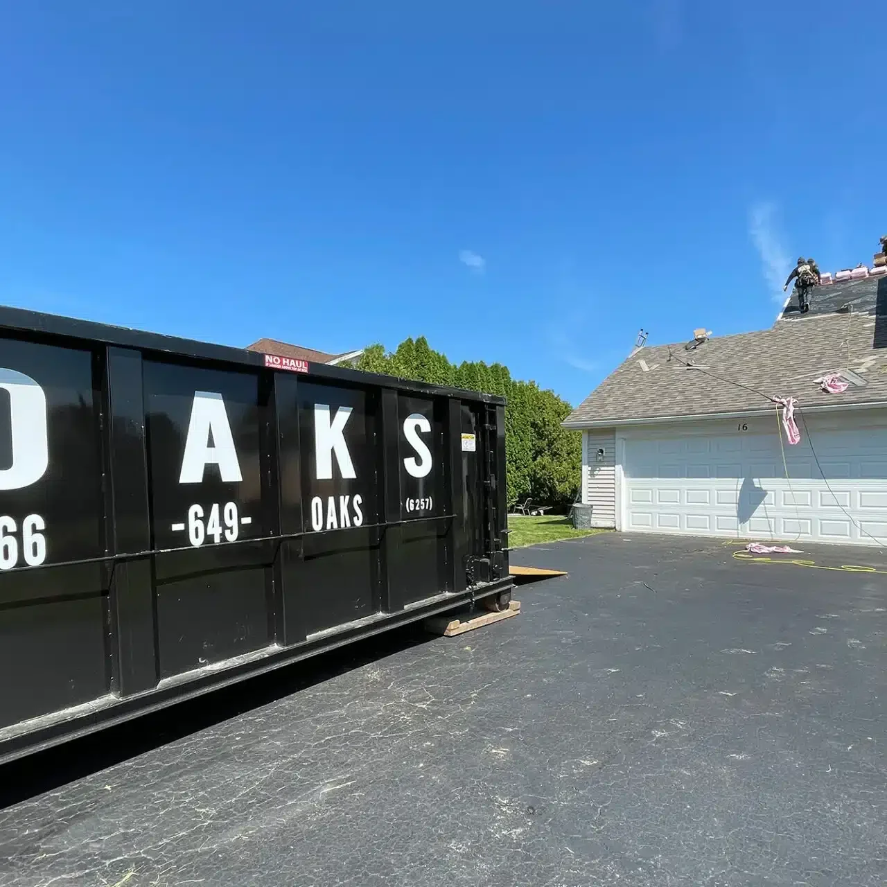 A large black dumpster with Oaks logo on residential property. Oaks provides waste removal services.