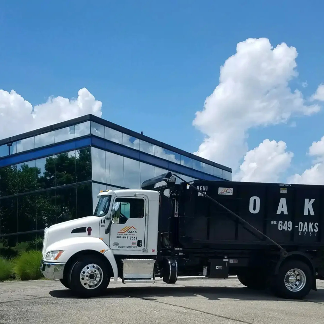 A white and black Oaks dump truck parked in front of a modern glass building.