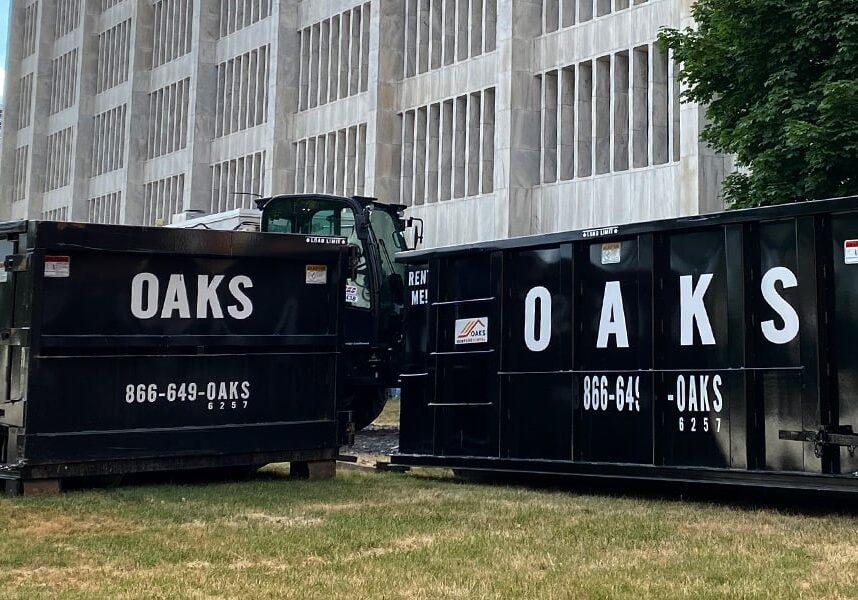 Two black dumpsters with Oaks logo on side